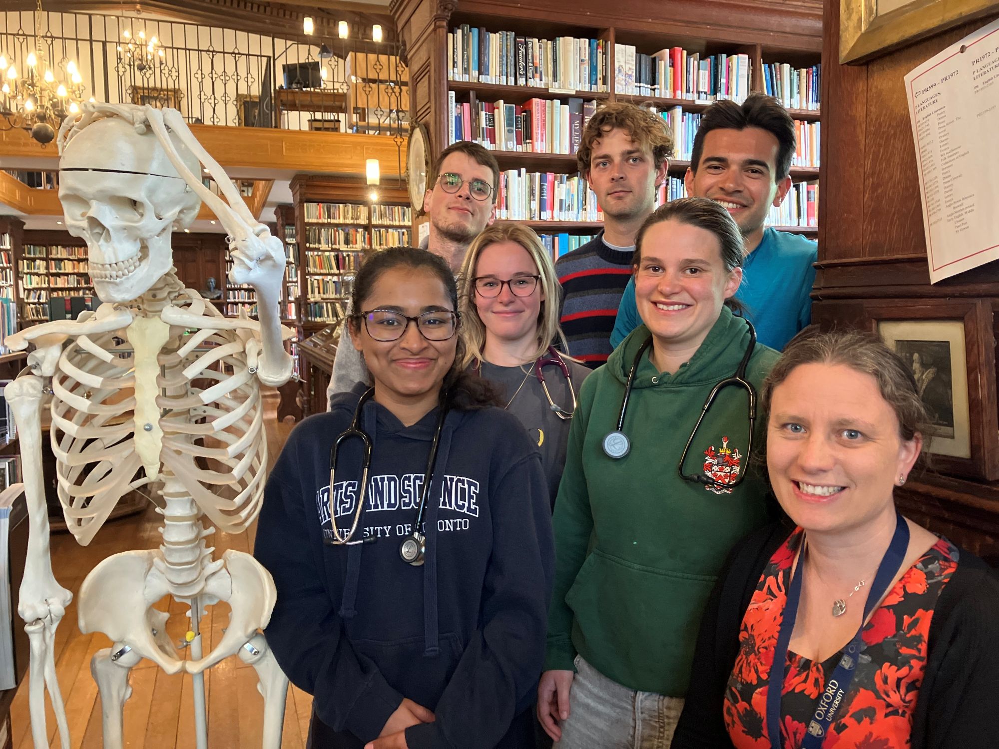 Students with stethoscopes in library next to model skeleton