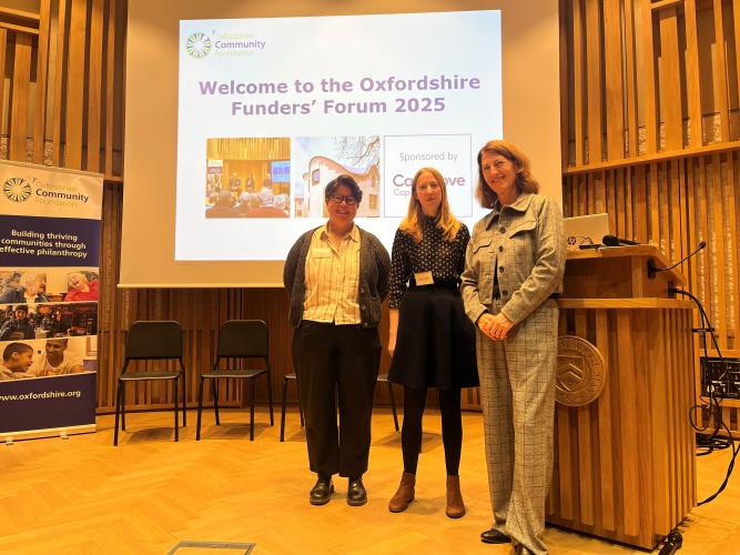 Three women stand on a stage in front of a projector screen