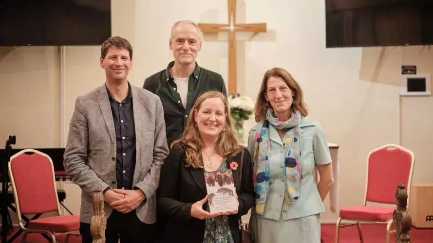 Two men and two women pose with one woman holding a book in her hand