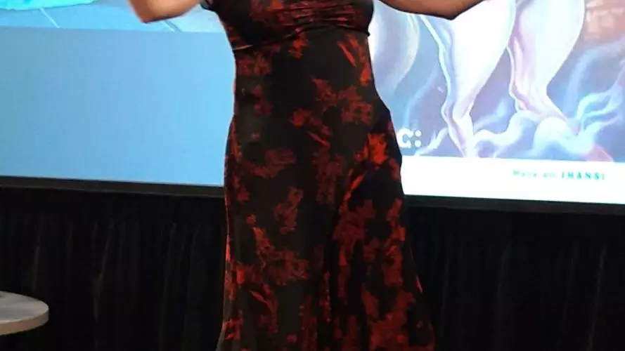 A woman on a stage gesturing enthusiastically