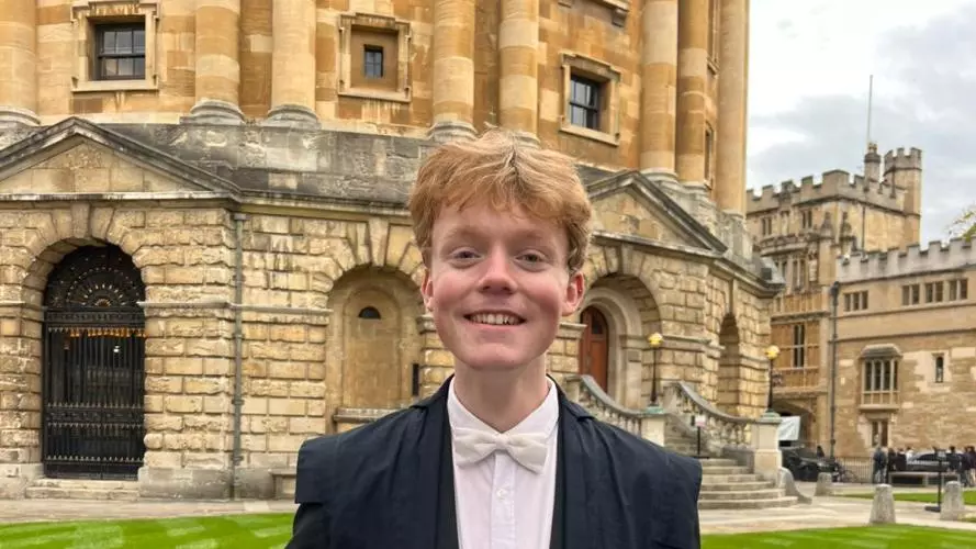 Photo of student in academic sub fusc in front of historic Radcliffe Camera building 