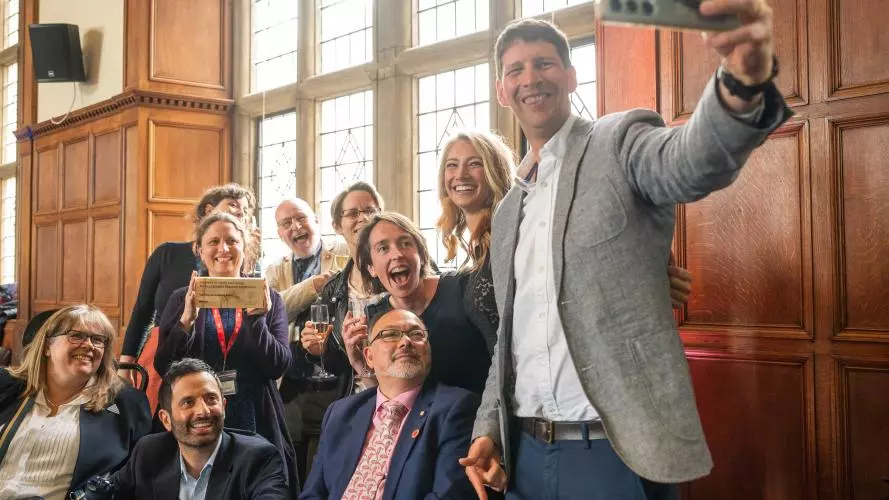 A group of people celebrate as one of the group takes a selfie and another holds up an award