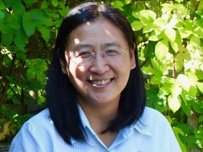 Photo portrait of Professor Bee Wee, smiling against a backdrop of green foliage
