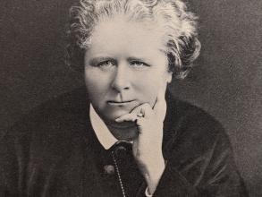A black and white portrait of a female head and shoulders shot.  The women is resting her chin on her hand, looking into the middle distance.