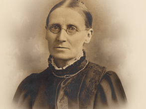 Black and white headshot photo of Lucy Toulmin Smith.  The sitter has her hair back, is wearing glasses and dressed in dark clothes.