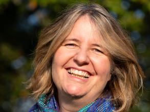Professor Sophie Park wearing a blue scarff and a black top, posing in front of greenery.