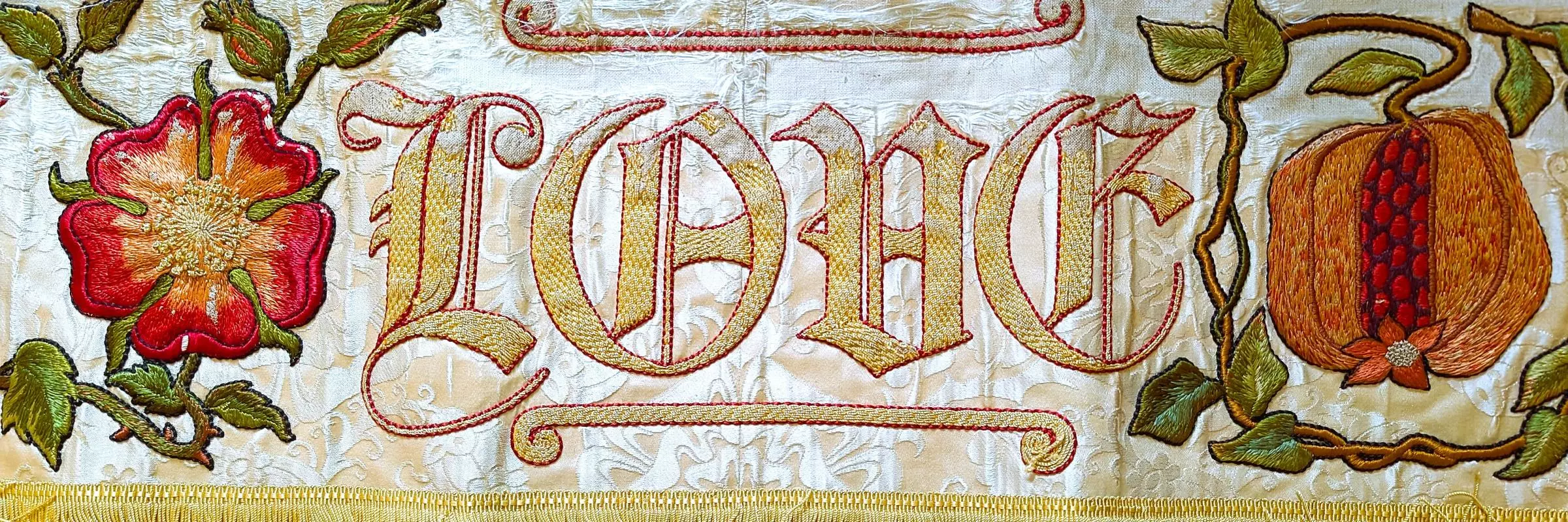Embroidered piece of cloth showing the word Love as well as two flowers and some foliage